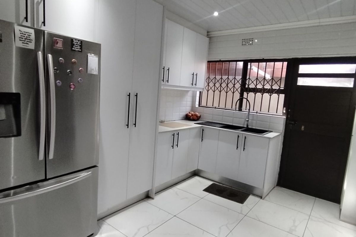 Modern kitchen featuring white cabinetry, marble-look floor tiles, a double sink, and a secure exterior door with security gate.