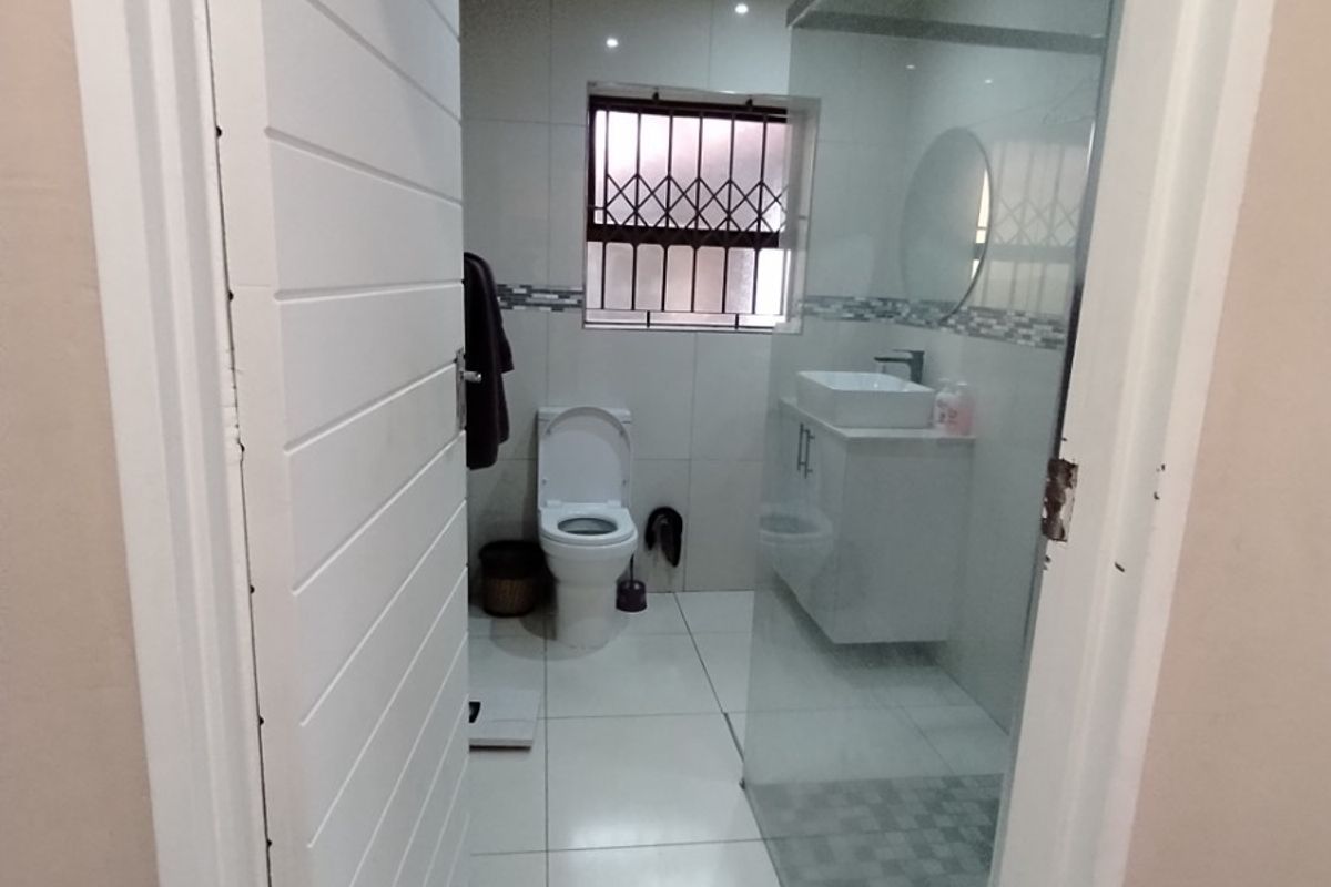Modern bathroom featuring a glass shower enclosure, vanity with vessel sink, tiled flooring, and a window with a security gate.