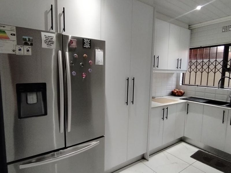 Modern kitchen featuring white cabinetry, tiled flooring, and a window with a security gate, providing a clean and functional workspace.