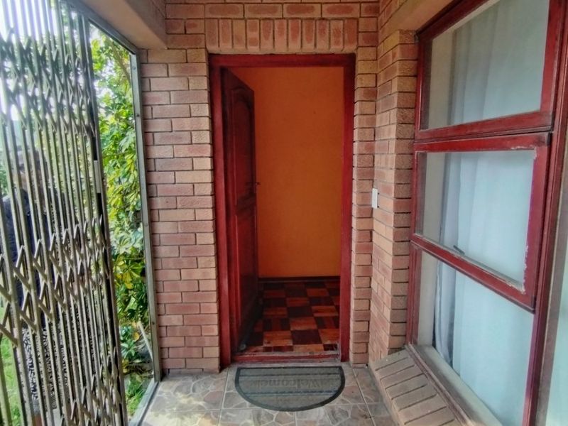 A covered entrance porch featuring exposed brick walls, tiled flooring, and a security gate leading to the main front door.