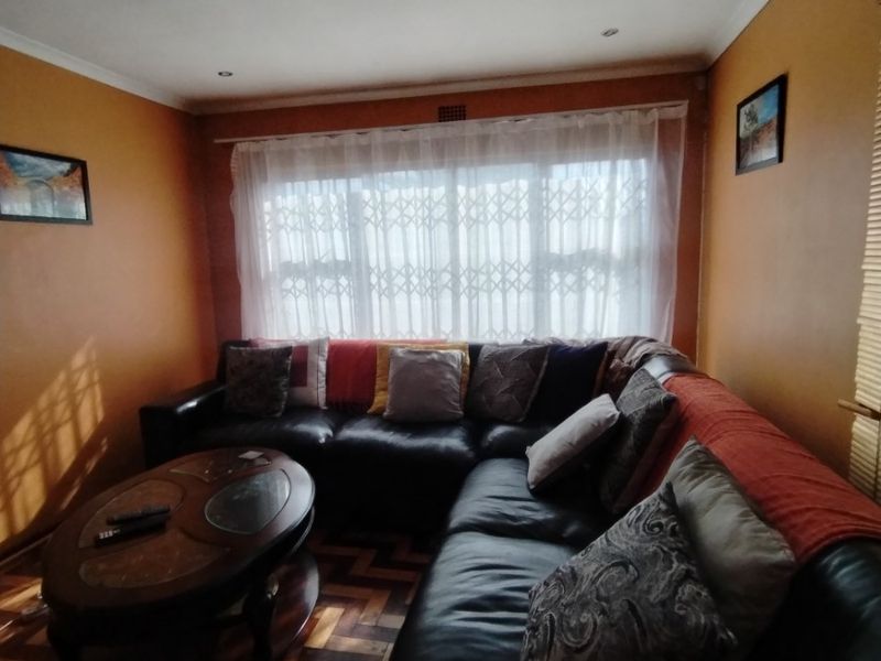 A living room featuring classic parquet flooring, a large window with a security gate, and warm-toned walls.
