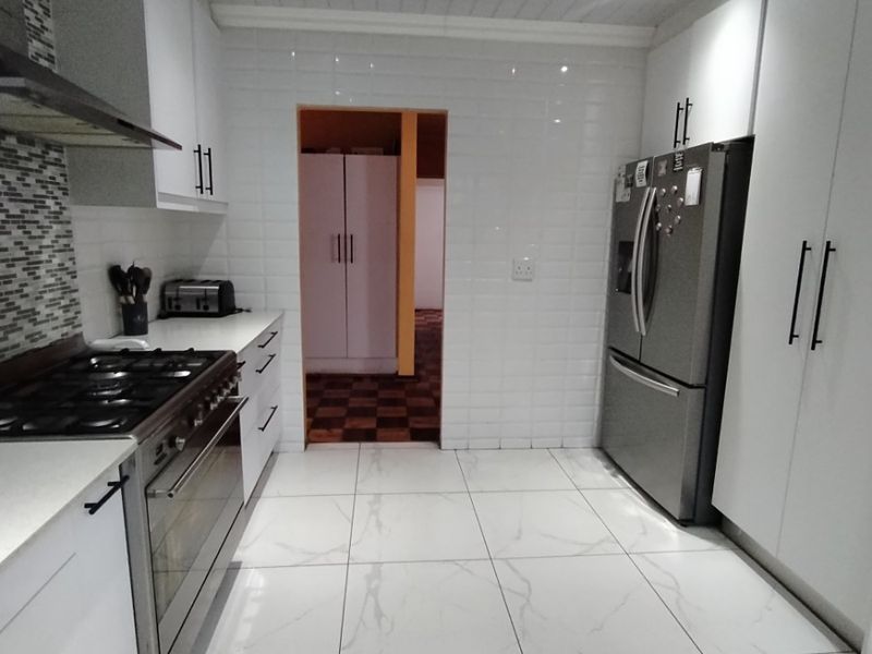 Modern kitchen featuring white cabinetry, subway tile backsplash, marble-look floor tiles, and a stainless steel gas stove with extractor fan.