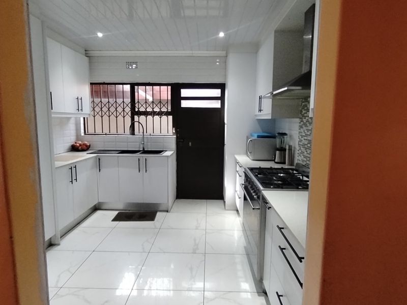 Modern kitchen featuring white cabinetry, gas hob, extractor fan, double sink, and polished tiled flooring with direct access to the exterior.