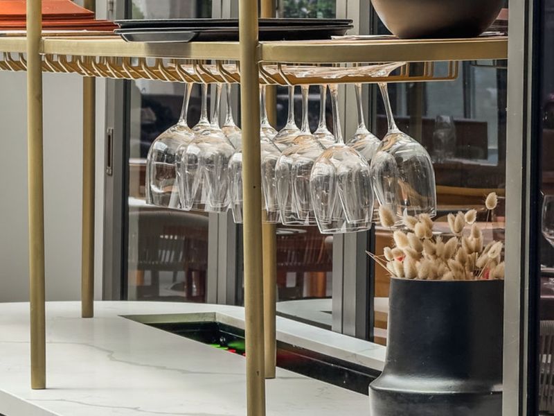 A modern bar area featuring a sleek stone countertop and a brass-finished overhead glass rack, set against large sliding glass doors.