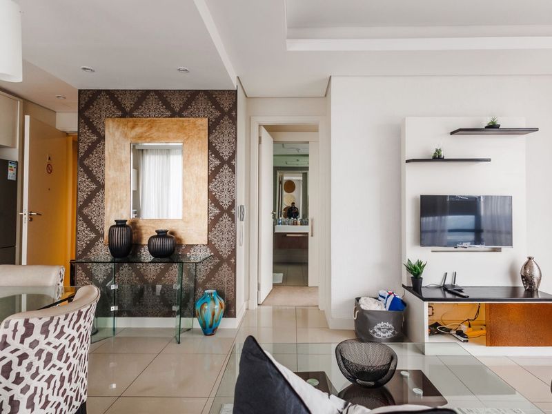 A well-maintained living area featuring a modern built-in media console, decorative wallpaper feature wall, and neutral porcelain floor tiles with recessed ceiling lighting.