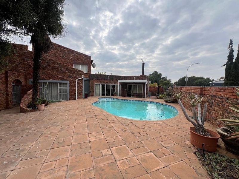 Spacious rear garden area featuring a swimming pool, extensive paved patio, and traditional face-brick exterior architecture.