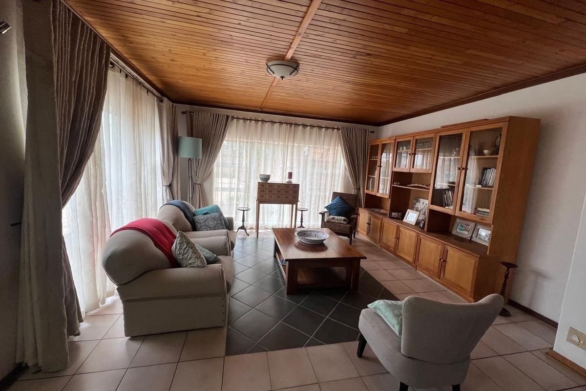 A spacious living room featuring a warm timber tongue and groove ceiling, tiled flooring, and extensive built-in cabinetry for storage.