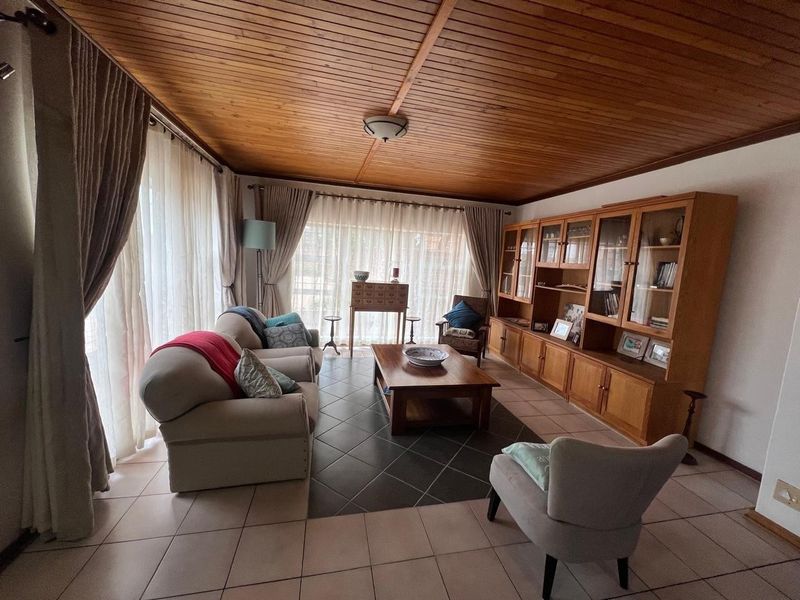 A spacious living room featuring a warm timber tongue and groove ceiling, tiled flooring, and extensive built-in cabinetry for storage.