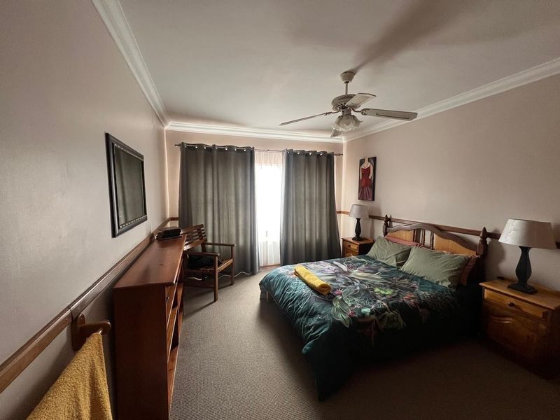A carpeted bedroom featuring a ceiling fan, crown molding, and a wooden dado rail, providing a functional and comfortable sleeping space.