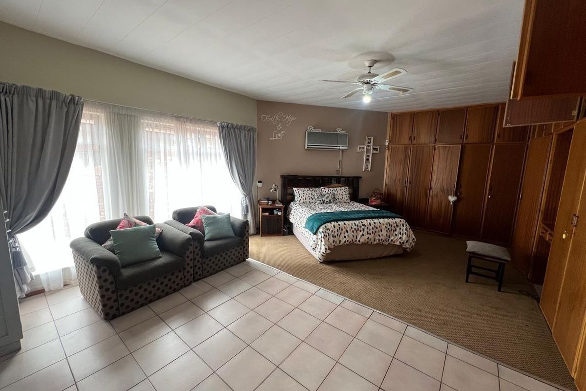 Spacious bedroom featuring built-in wooden cupboards, a ceiling fan, wall-mounted air conditioning, and a combination of tiled and carpeted flooring.
