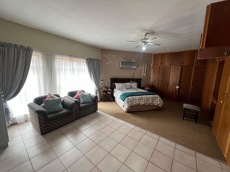Spacious bedroom featuring built-in wooden cupboards, a ceiling fan, wall-mounted air conditioning, and a combination of tiled and carpeted flooring.