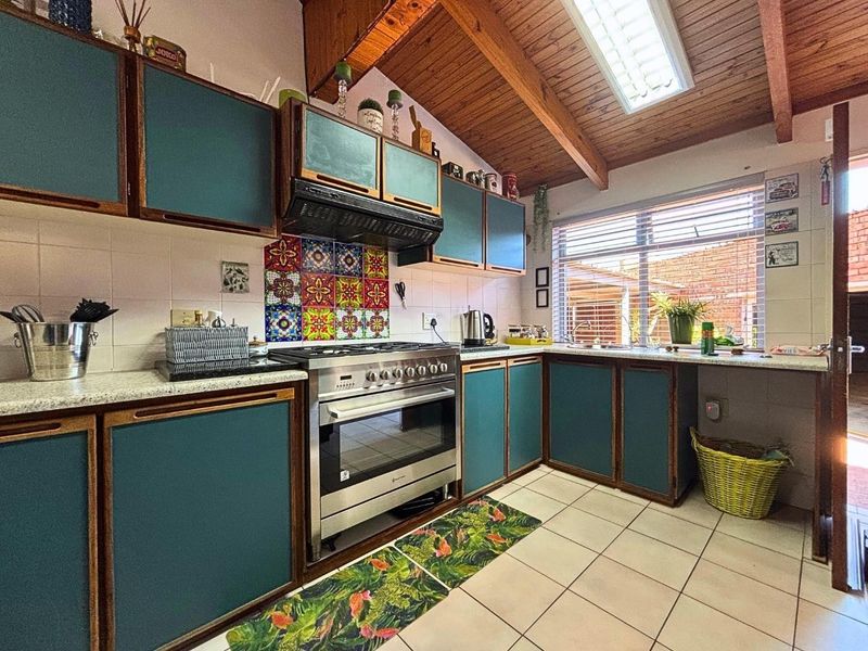 A kitchen featuring timber vaulted ceilings, a skylight, tiled flooring, and a gas stove with a decorative tiled backsplash.