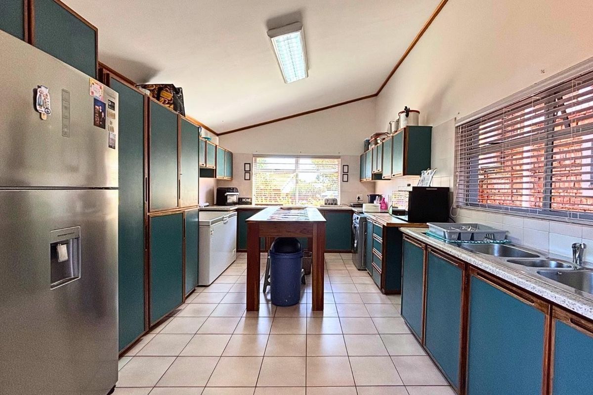A functional kitchen featuring extensive built-in cabinetry, tiled flooring, and a double bowl sink, offering a practical layout with ample storage space.