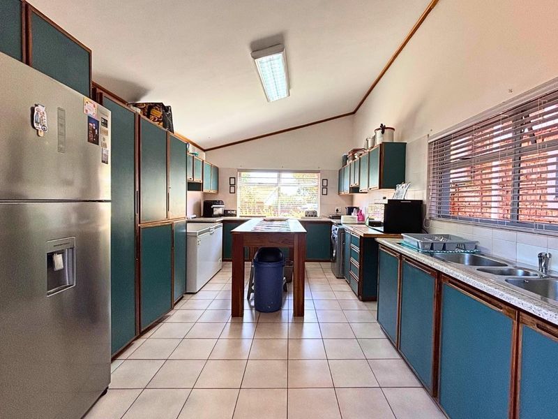 A functional kitchen featuring extensive built-in cabinetry, tiled flooring, and a double bowl sink, offering a practical layout with ample storage space.