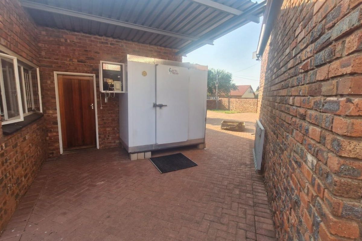 A paved rear courtyard area featuring exposed brick walls, a covered section with a corrugated roof, and a built-in cold storage unit.