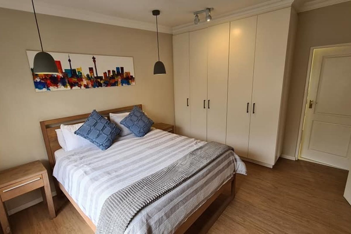 A well-maintained bedroom featuring neutral walls, laminate flooring, and ample built-in cupboard storage with modern pendant lighting.