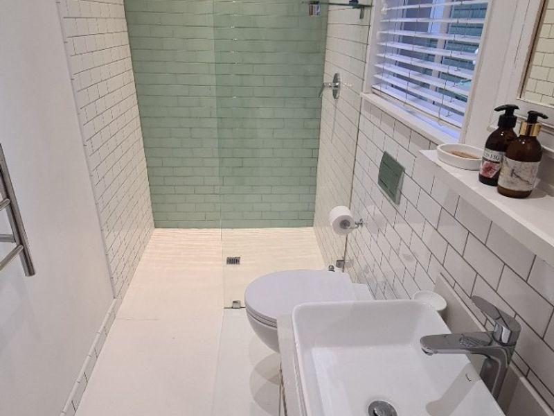 Modern bathroom featuring a walk-in shower with green subway tiles, a white vessel sink, wall-mounted toilet, and a heated towel rail.