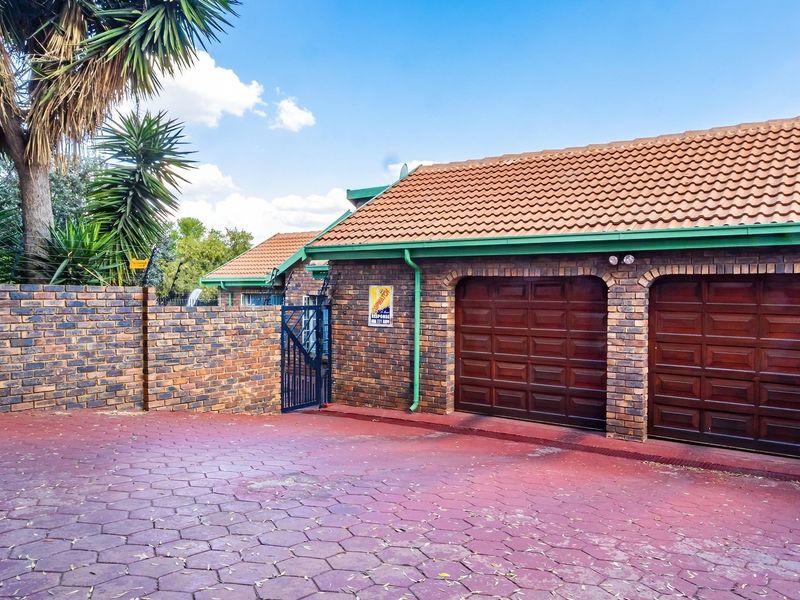 Front exterior view of the property featuring a double garage with wooden doors, a paved driveway, and a secure brick boundary wall.