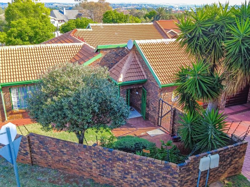 Aerial view of a face brick residential property featuring a tiled roof, paved driveway, and secure perimeter wall with electric fencing.