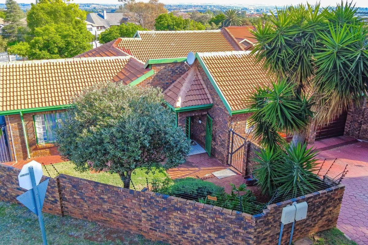 Aerial view of a face brick residential property featuring a tiled roof, paved driveway, and secure perimeter wall with electric fencing.
