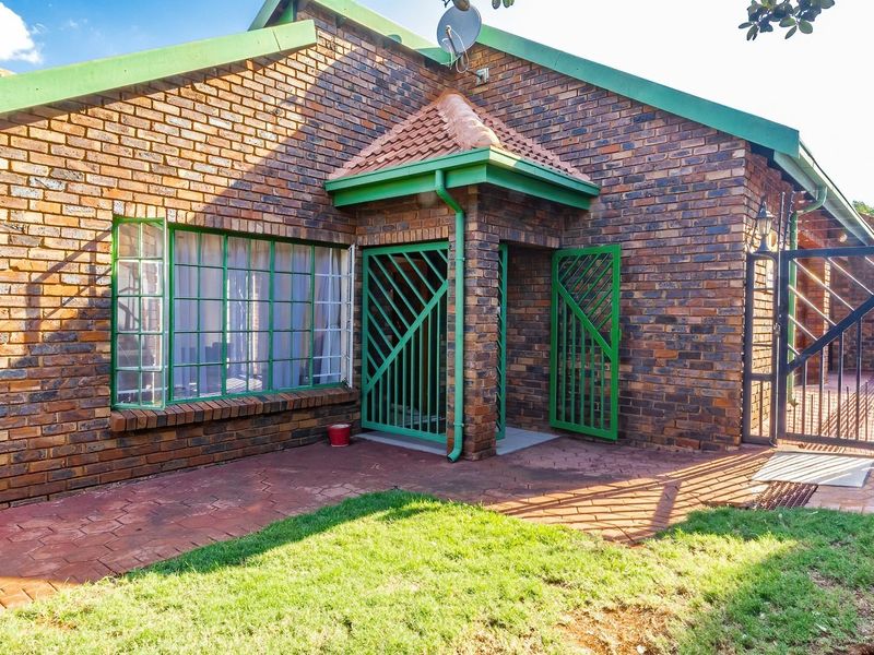 Rear view of a face brick house featuring a paved patio area, secure metal gates, and perimeter electric fencing.
