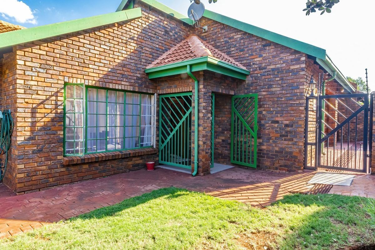 Rear view of a face brick house featuring a paved patio area, secure metal gates, and perimeter electric fencing.