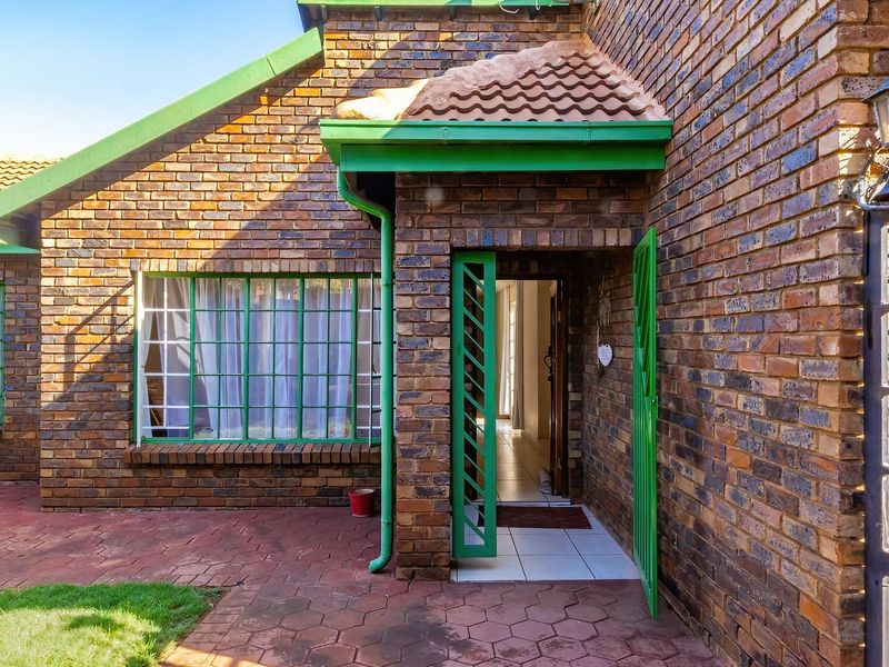 Front entrance of a face brick house featuring a paved patio area, security gate, and green metal window frames.