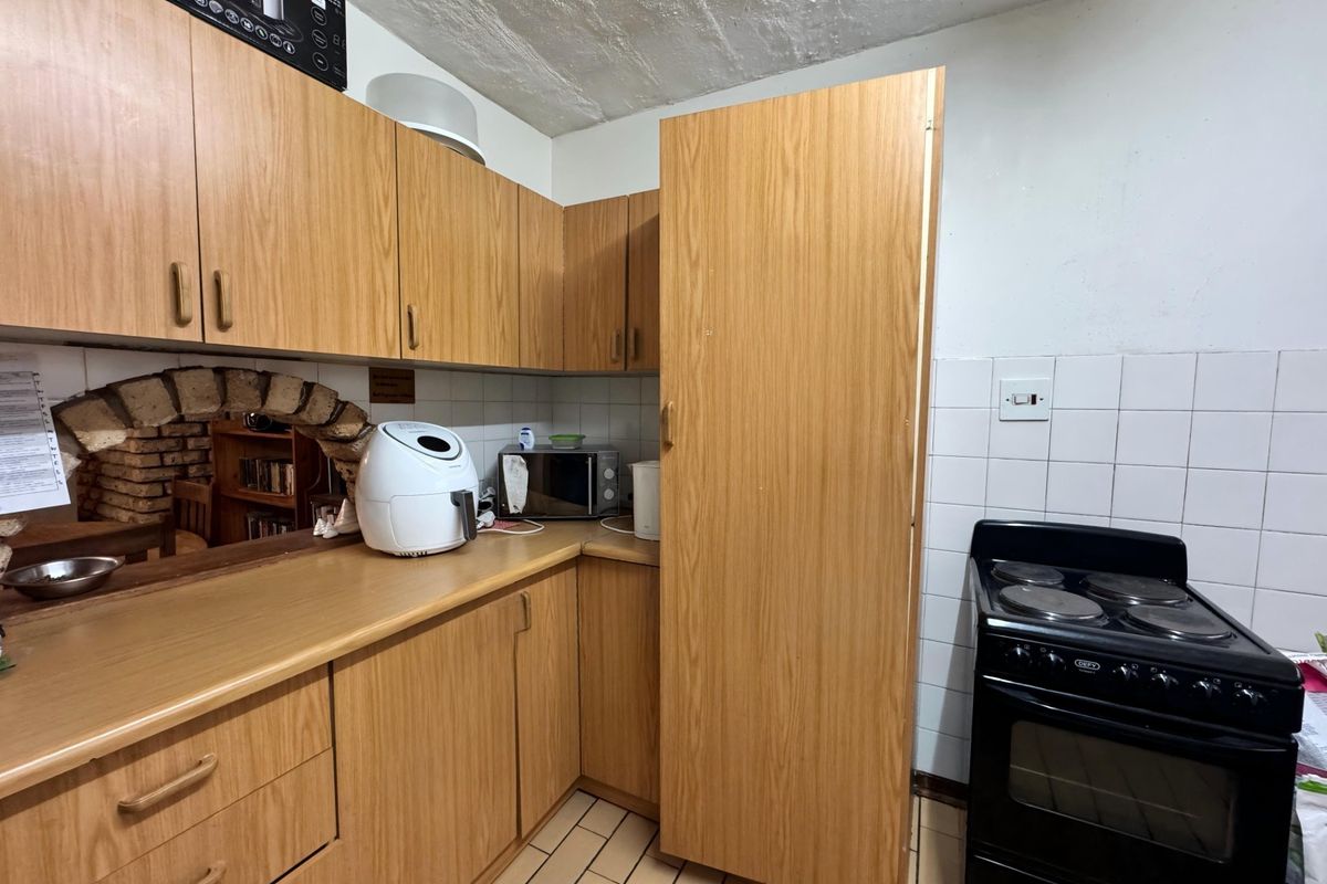 A functional kitchen featuring wood-look laminate cabinetry, tiled backsplash, and a freestanding electric stove, offering potential for modernization.