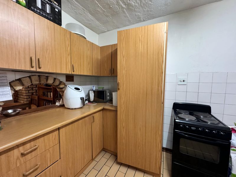 A functional kitchen featuring wood-look laminate cabinetry, tiled backsplash, and a freestanding electric stove, offering potential for modernization.
