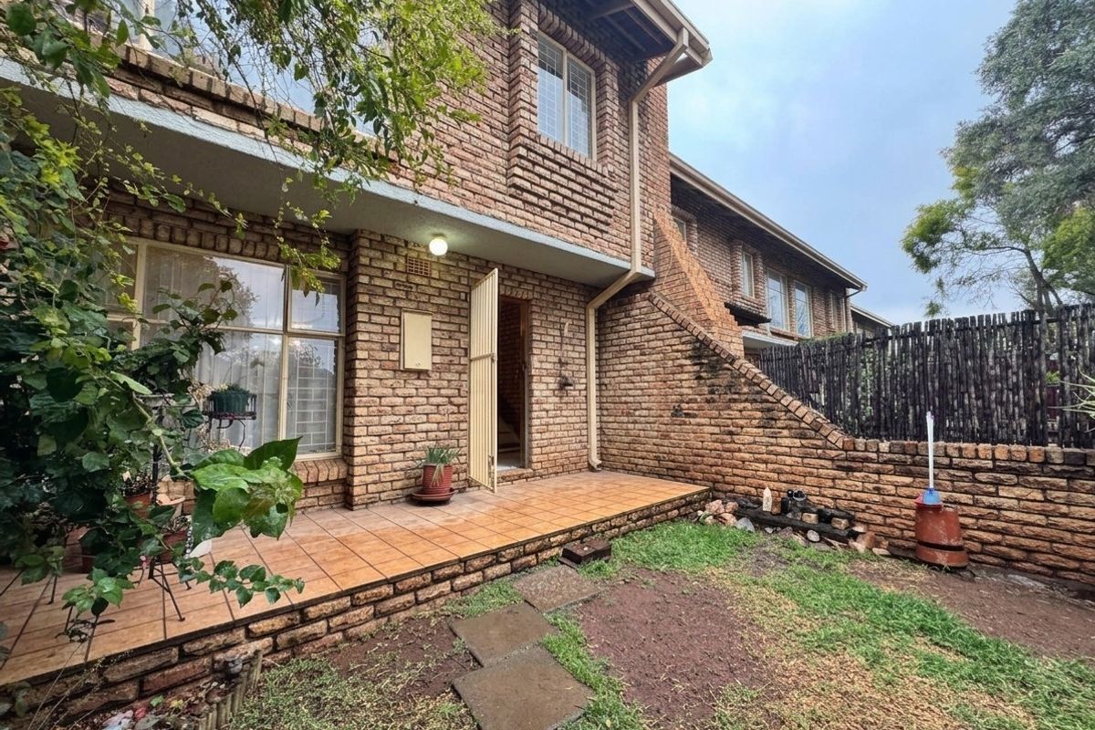 Rear exterior view of a face brick townhouse featuring a tiled patio area, security gate, and a small private garden space.