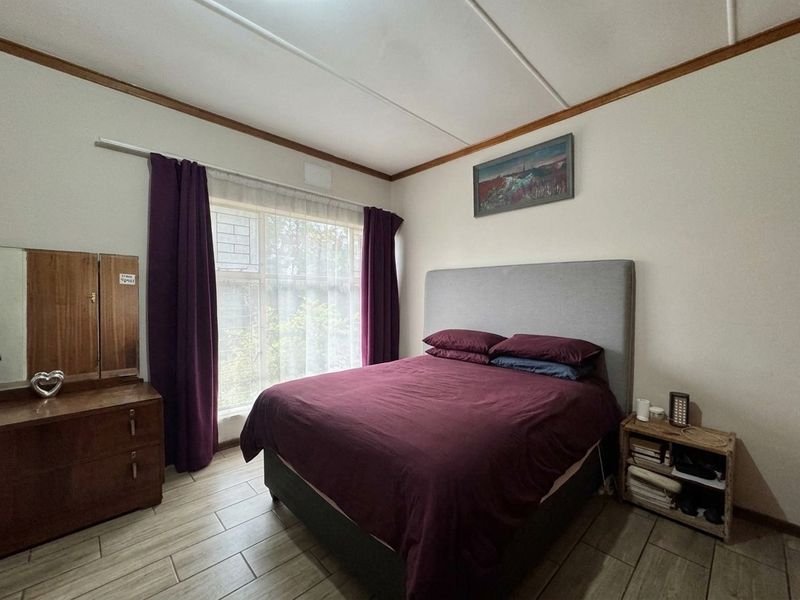 A functional bedroom featuring tiled flooring, a large window with security bars, and neutral wall finishes.