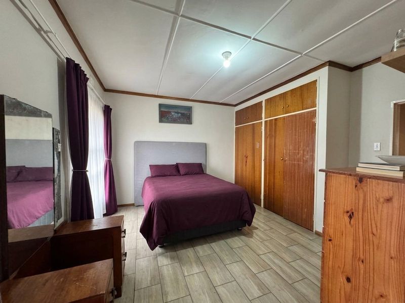 A functional bedroom featuring tiled flooring, a panelled ceiling, and built-in wooden cupboards providing ample storage space.