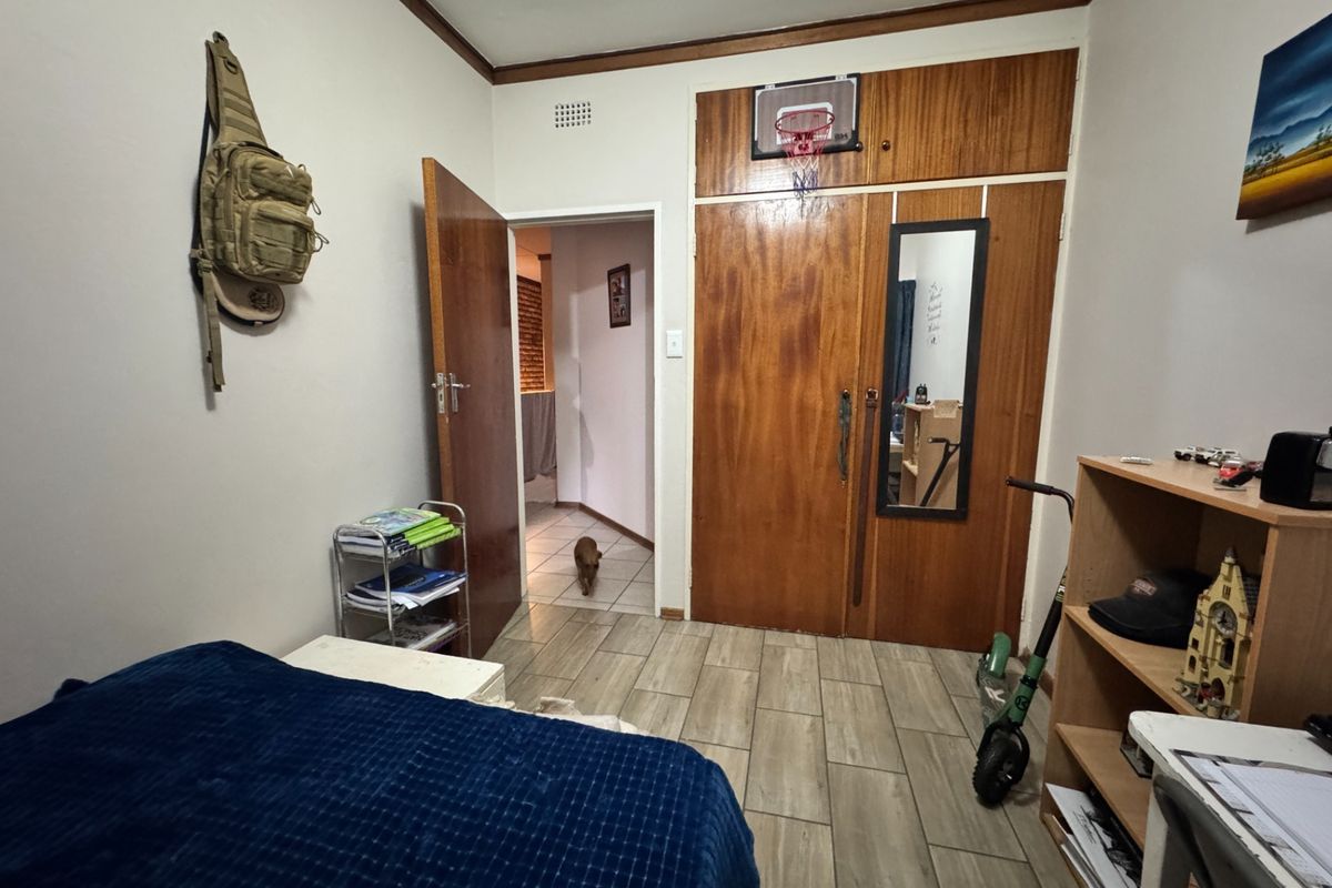 A bedroom featuring built-in wooden cupboards, tiled flooring, and a doorway leading to an adjacent hallway.