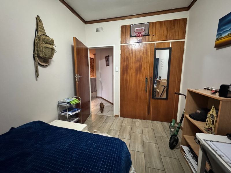 A bedroom featuring built-in wooden cupboards, tiled flooring, and a doorway leading to an adjacent hallway.