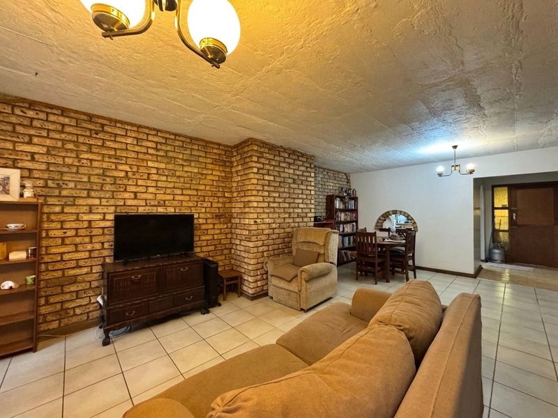 Open plan living and dining area featuring an exposed brick wall, ceramic floor tiles, and a textured ceiling with traditional lighting fixtures.
