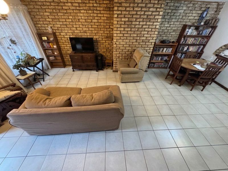 A living room featuring an exposed brick feature wall and neutral ceramic floor tiles, offering a functional and dated living space.