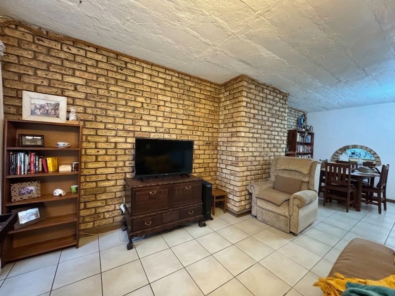 Open plan living and dining area featuring a prominent exposed brick feature wall, tiled flooring, and a textured concrete ceiling.