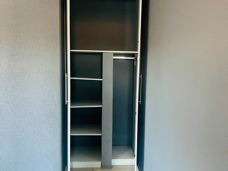 A bedroom featuring a built-in wardrobe with shelving and hanging space, complemented by crown molding and neutral tiled flooring.