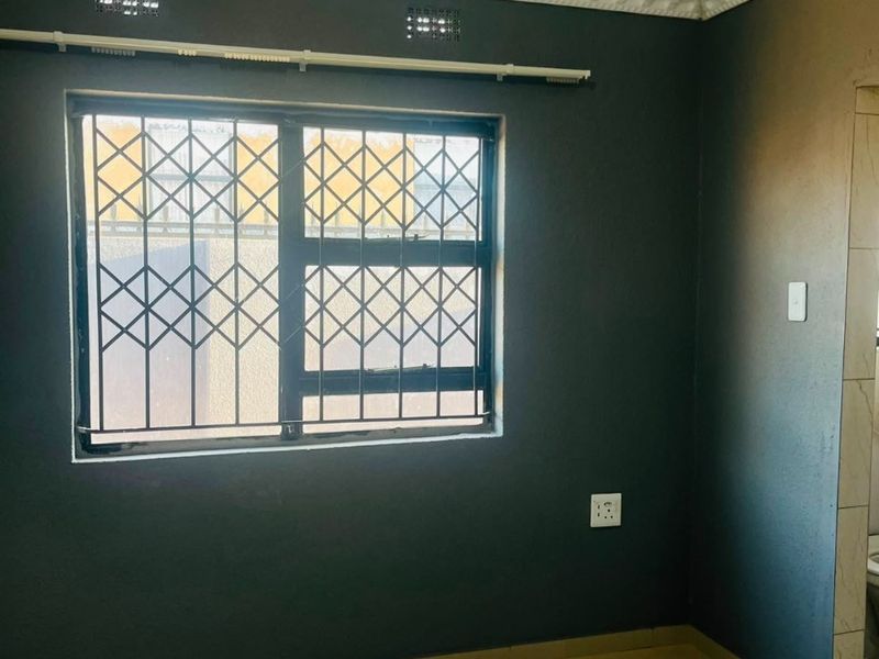An empty bedroom featuring dark painted walls, tiled flooring, decorative cornice, and a window fitted with a security gate.