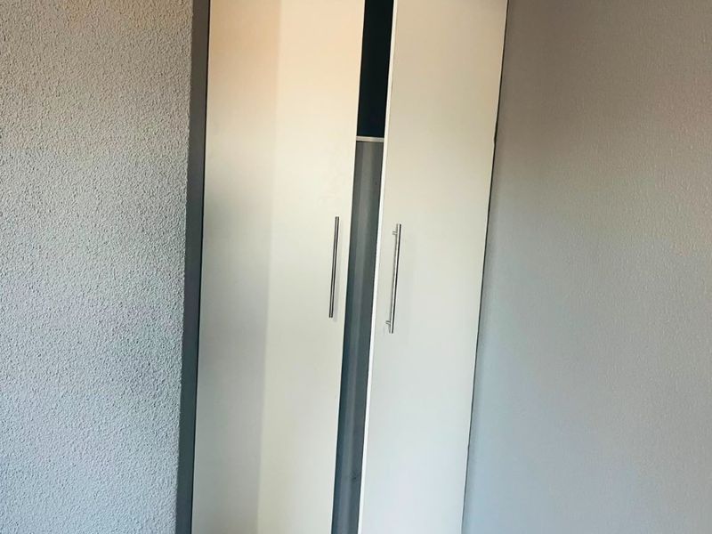 A bedroom corner featuring a built-in white wardrobe with modern handles, crown molding, and neutral tiled flooring.