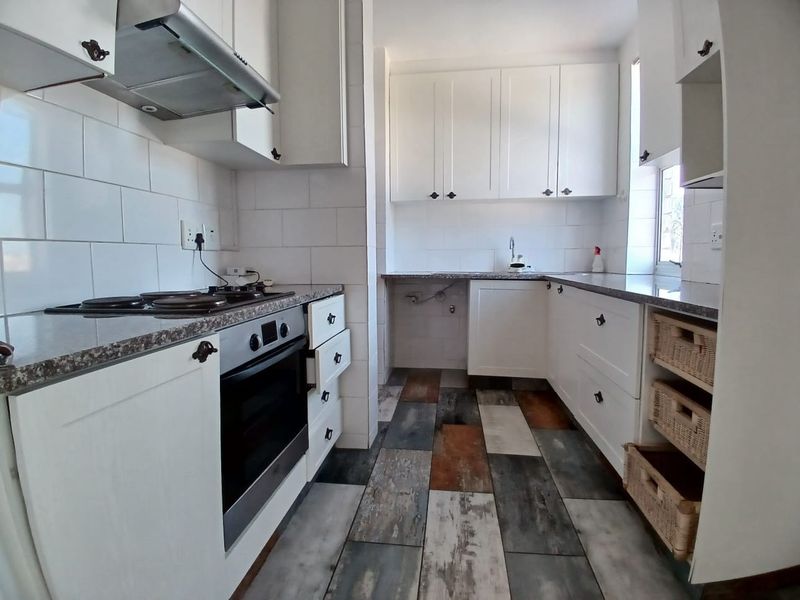 A functional kitchen featuring white cabinetry, granite countertops, subway tile backsplash, and integrated appliances with a distinctive multi-toned tiled floor.