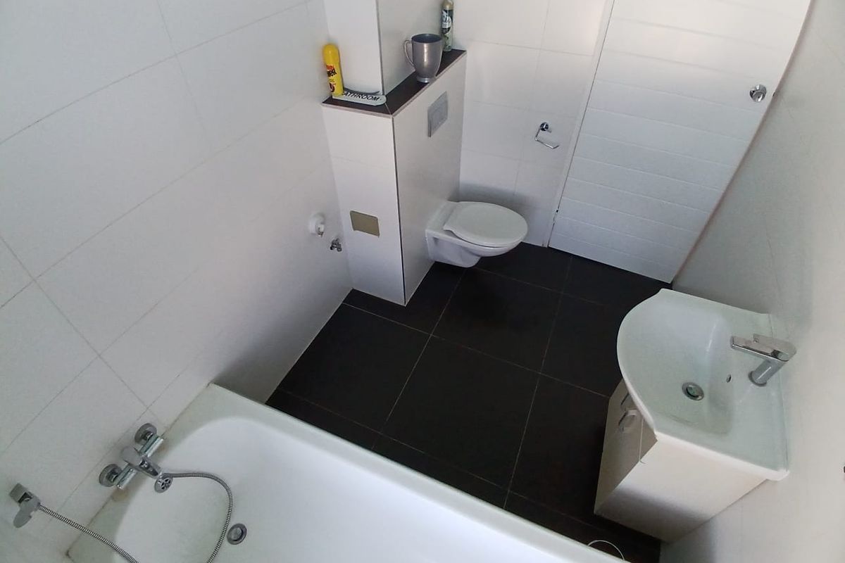 A modern bathroom featuring a wall-hung toilet with a concealed cistern, a bathtub with a handheld shower mixer, and a vanity basin.