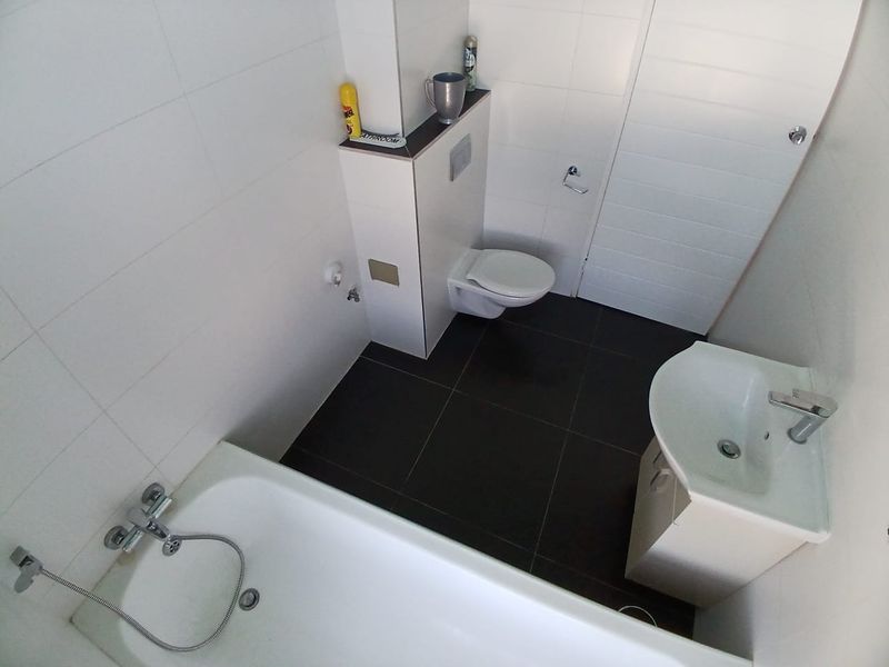 A modern bathroom featuring a wall-hung toilet with a concealed cistern, a bathtub with a handheld shower mixer, and a vanity basin.