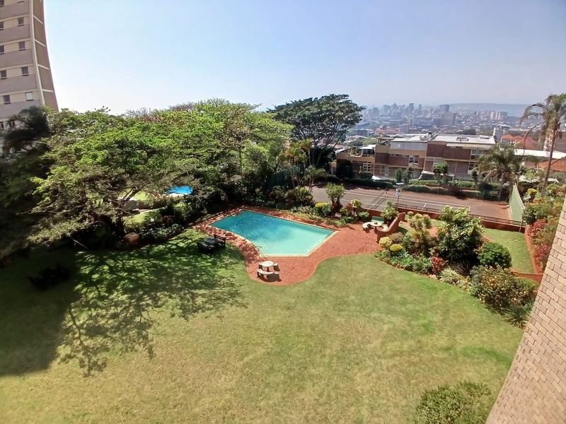 Elevated view of the apartment complex communal grounds, featuring a swimming pool, landscaped garden areas, and a tennis court.