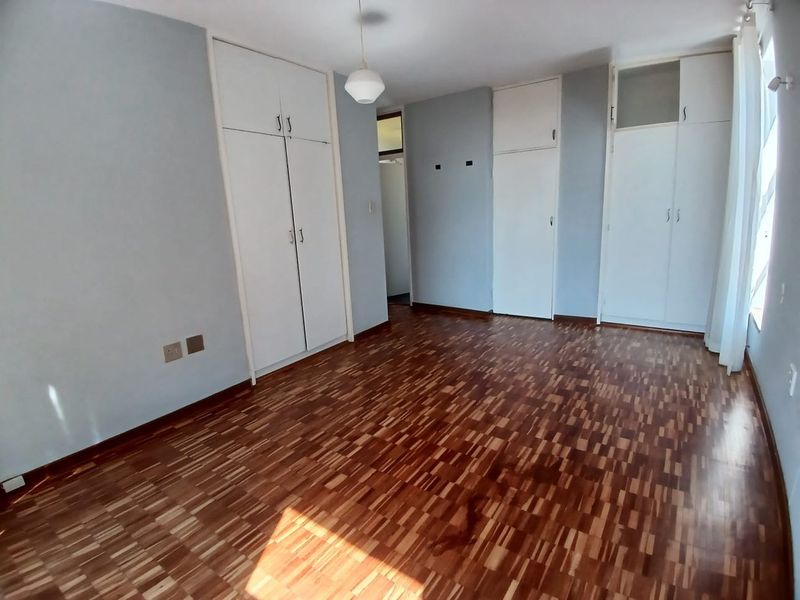 A bright, empty bedroom featuring classic parquet flooring and ample built-in cupboard storage, offering a clean canvas for personalization.