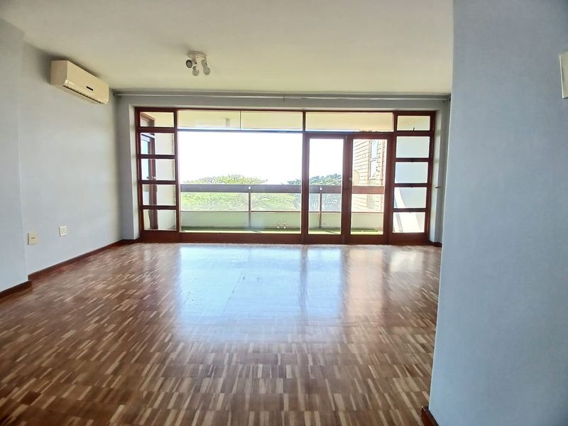 Spacious, light-filled living area featuring polished parquet flooring, a wall-mounted air conditioner, and large timber-framed glass doors leading to an outdoor balcony.