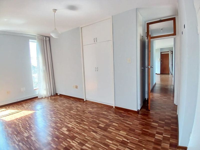 A bright, empty bedroom featuring classic parquet flooring, built-in cupboards, and a wooden door frame leading to the hallway.