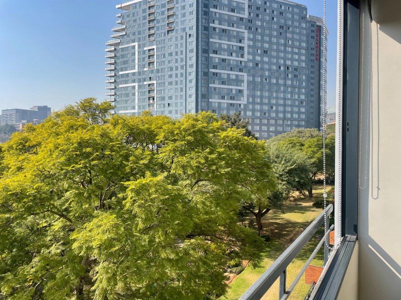 An elevated view from a balcony overlooking a lush green park and surrounding urban high-rise buildings.