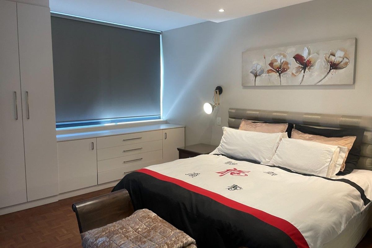 A well-maintained bedroom featuring parquet flooring, built-in cabinetry, a large wardrobe, and recessed downlighting with a modern roller blind.