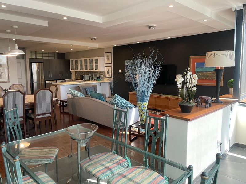 Spacious open-plan living and dining area featuring a modern kitchen with island, recessed ceiling lighting, and a blend of hardwood and tiled flooring.
